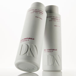 Two white cylindrical bottles of Daily Naturals Everyday Balancing Conditioners on a reflective white surface, with one bottle standing upright and the other tilted in front showing the embossed DN logo.