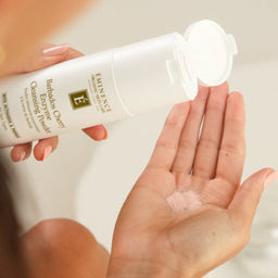 A person holds a white bottle of Elevation Skincare Salicylic Acid Cleansing Foam and squeezes foam into their palm, with a small bowl of red berries blurred in the background.