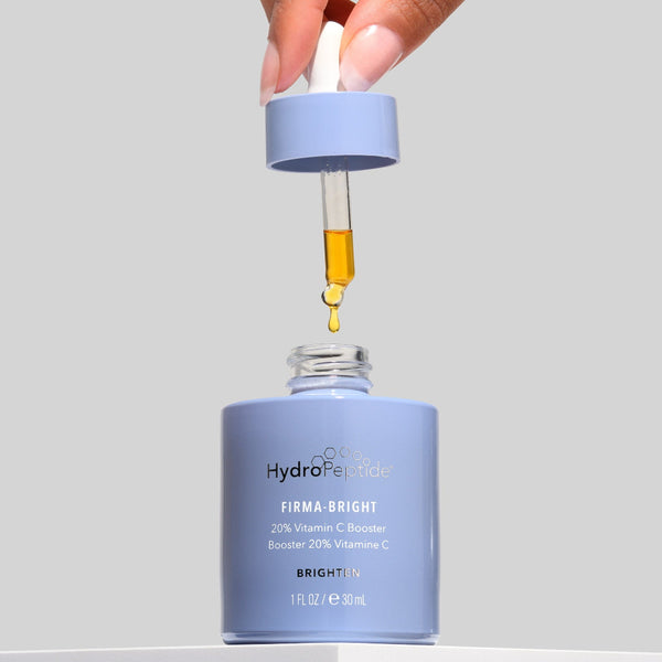 Hand holding a dropper over a blue skincare bottle labeled 'HydraPeel' on a gray background
