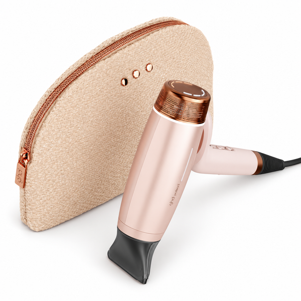 A rose gold hair dryer with a black concentrator nozzle, shown next to its matching textured beige zippered carrying case on a white background.
