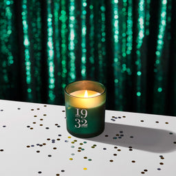 Green candle with '1932' on a white surface with confetti, against a green matrix background.