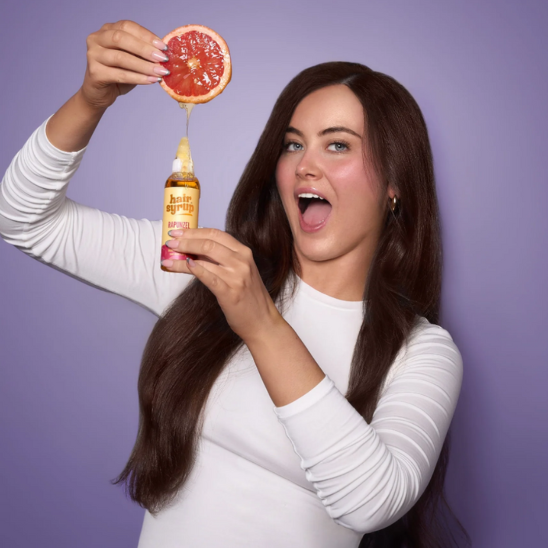 Woman holding a bottle of grapefruit syrup with a purple background