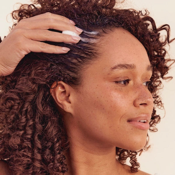 Woman applying product to her hair with a neutral background