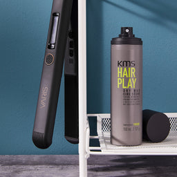 Hair straightener and KMS Hair Play product on a white surface with a blue wall background
