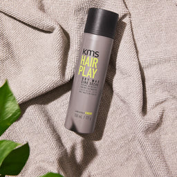 KMS Hair Play product on a textured surface with leaves in the corner