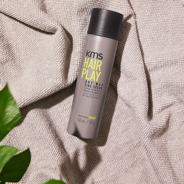 KMS Hair Play product on a textured surface with leaves in the corner