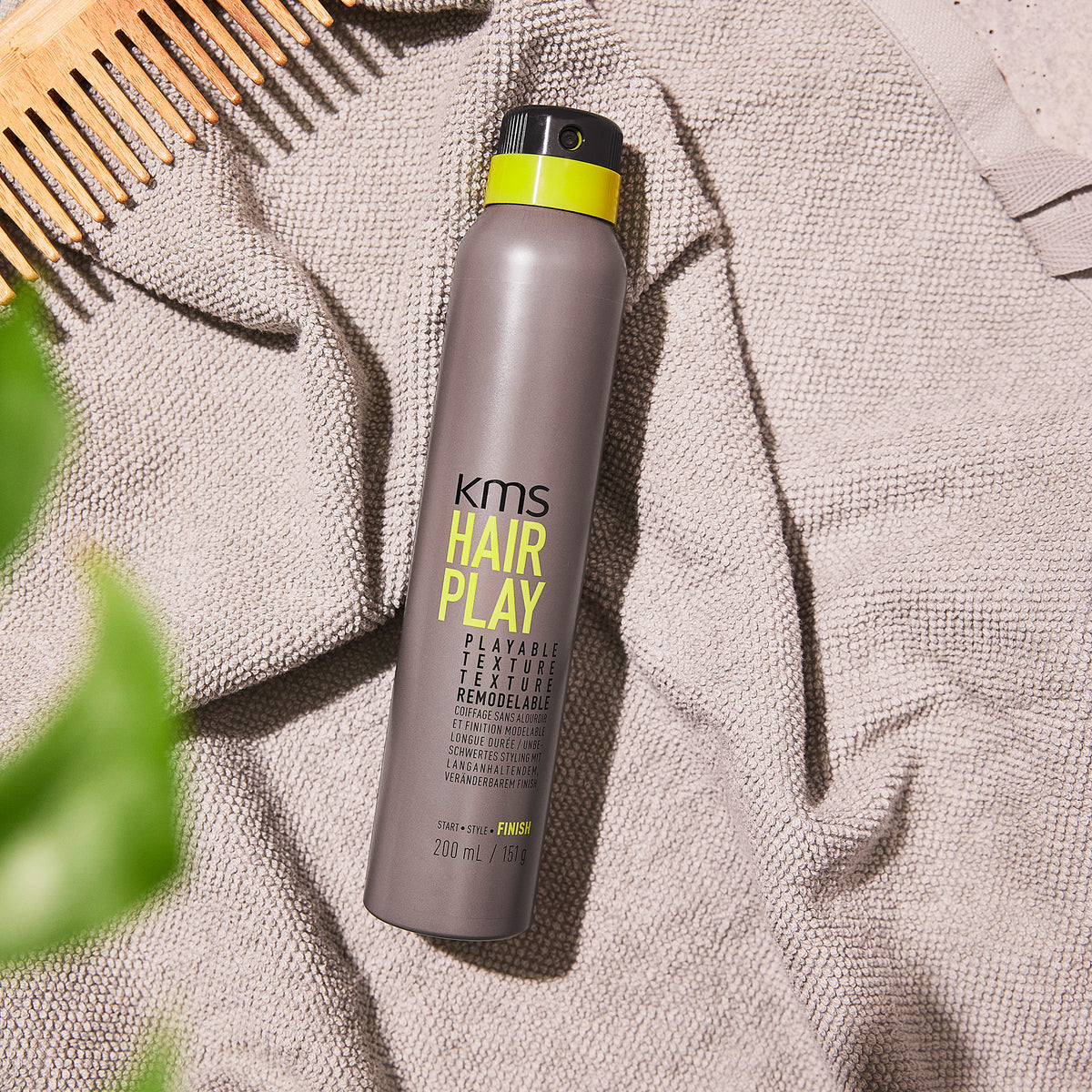 KMS Hair Play product on a towel with a comb and green leaves in the background