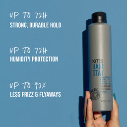 KMS Hair Stay product bottle held by a hand with text on a blue background