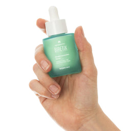 Hand holding a Biretix skincare dropper bottle against a white background