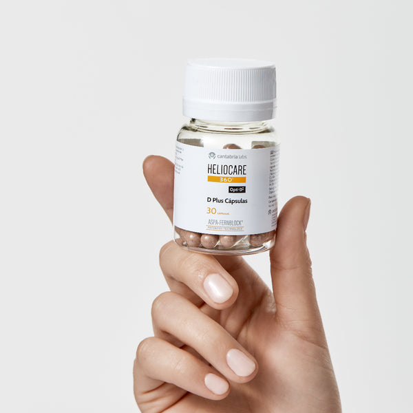 Hand holding a bottle of Heliocare supplements against a light background