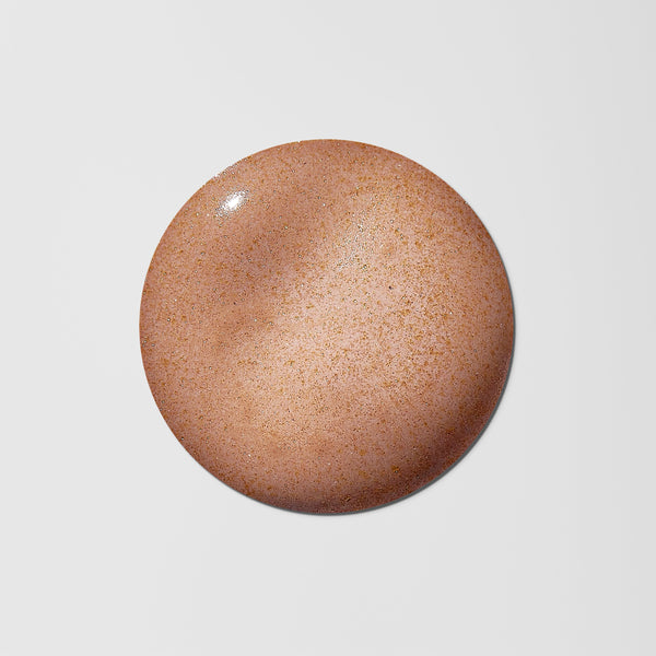 A circular swatch of warm tan-brown cosmetic cream or powder with fine speckling, centered on a light gray background.