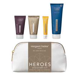 Margaret Dalb's Heroes Discovery Kit featuring four travel-sized toiletry tubes in purple, gold, yellow, and blue, arranged above a white zippered pouch with a brown label.