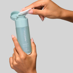 Person holding a blue skincare bottle with a gray background