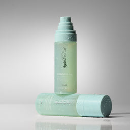 A light mint green bottle of HydroShower Resilience Shower Gel stands upright, with its matching cap lying horizontally in front on a reflective surface, set against a clean gray studio background.
