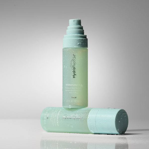 A light mint green bottle of HydroShower Resilience Shower Gel stands upright, with its matching cap lying horizontally in front on a reflective surface, set against a clean gray studio background.