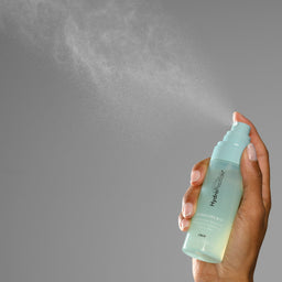 Hand holding a spray bottle labeled 'Hydrasource' against a gray background