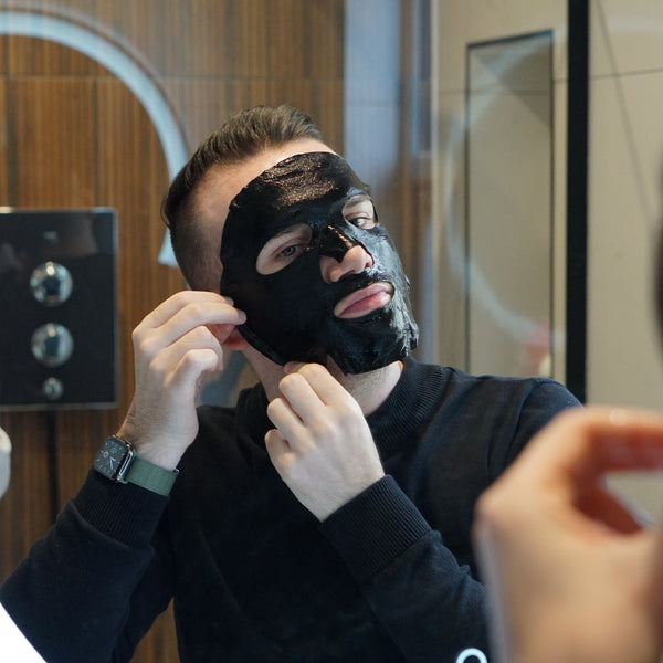 Man applying a black face mask in front of a mirror.
