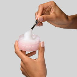 Person using a pink skincare product with a gray background