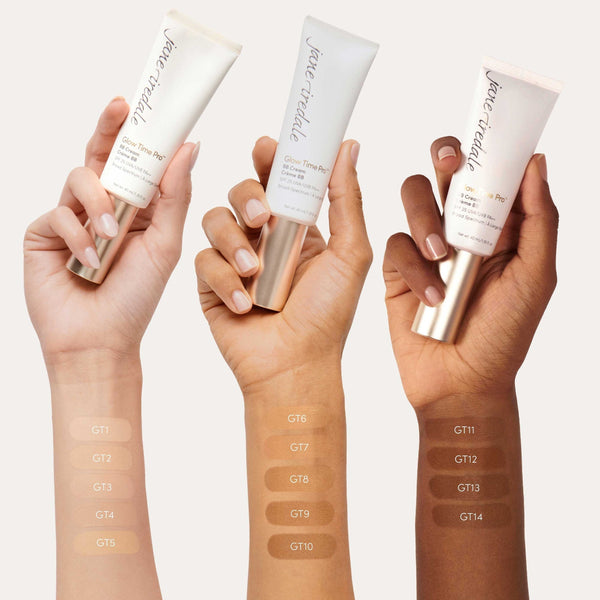 Three hands holding Jane Iredale foundation tubes with color swatches on a white background