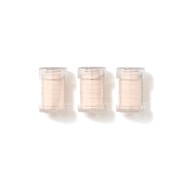 Three small clear plastic jars filled with a pale peach-beige textured powder, arranged side by side on a white background.