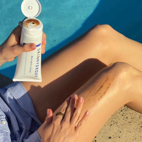 Person applying sunscreen to their leg by a pool