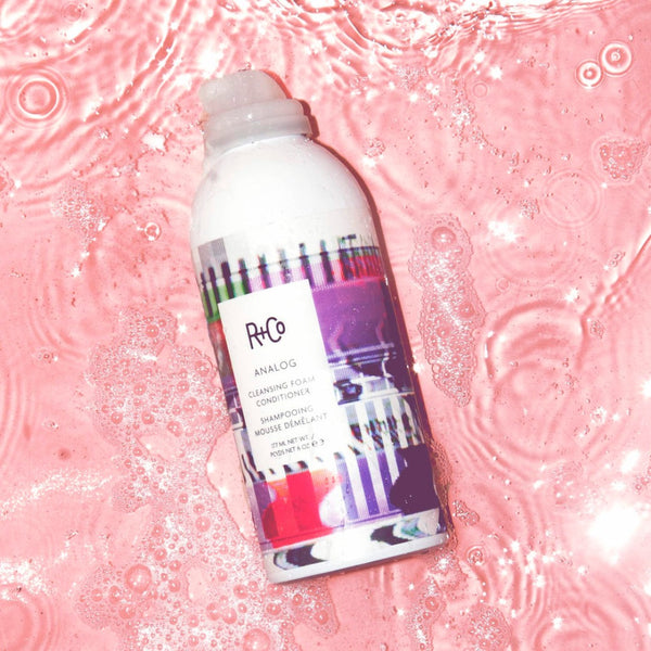 R+Co Analog Cleansing Foam Conditioner in a pool of pink water