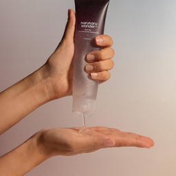 Hand holding a tube of haruharu wonder+ cleanser with clear gel being dispensed onto the palm.
