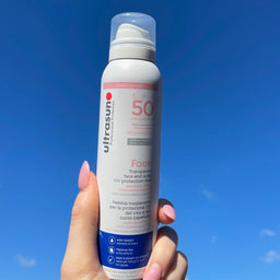 White Ultrasun UV Face & Scalp Mist SPF 50 150ml bottle in hand infront of sky
