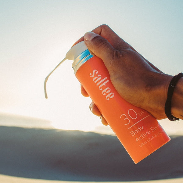a bottle of Saltee SPF30 Body Active Sun Lotion being used on a beach