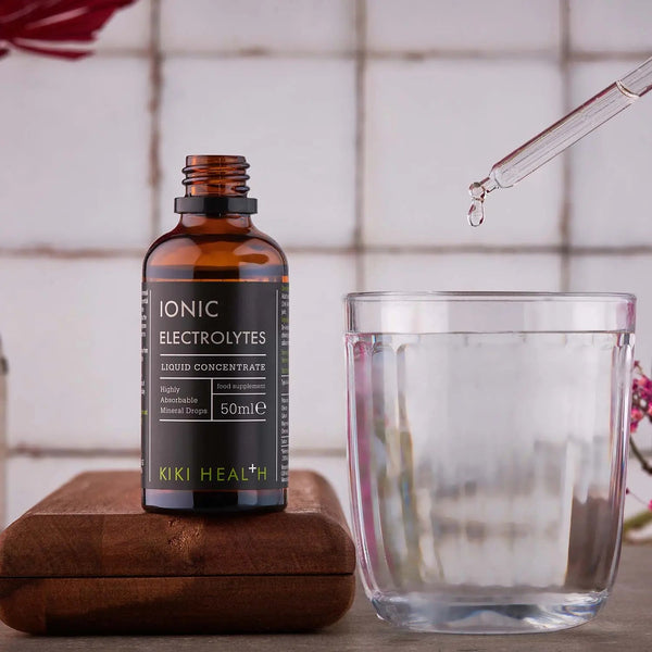 Kiki Health Ionic Electrolytes bottle with a glass and dropper on a wooden block.