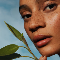 Close-up of a person holding a leaf against a blue sky