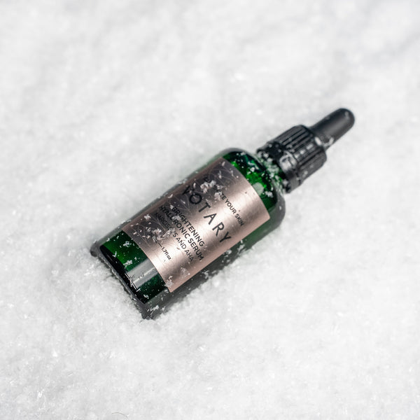 A small green glass dropper bottle labeled Botary Botanicals Gut Healing Salve, lying in white snow.