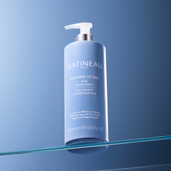 A bottle of Gatineau Paris Renewal Ultime AHA Body Wash, 400ml, standing on a reflective glass surface against a blue gradient background.