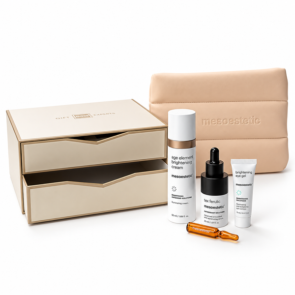 Mesoestetic skincare gift set featuring a beige double-drawer box, a beige zippered pouch, a white bottle of age element brightening cream, a black dropper bottle of tea kinase serum, a white tube of brightening mask, and two amber ampoules, arranged on a white background.