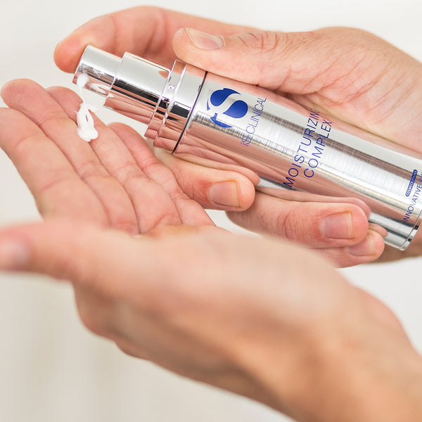 Silver skincare bottle with blue logo held in a hand against a white background