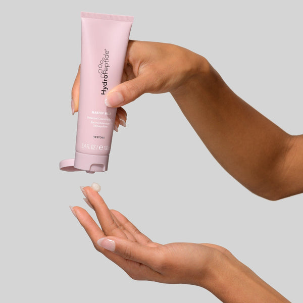 Hand holding a pink tube labeled 'CeraVe Hydro Peptide' against a gray background