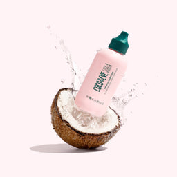 Coco & Eve Like A Virgin Miracle Hair Elixir bottle bouncing out of a coconut