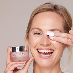 Woman applying cream to her face with a GATINEAU jar in front of her.
