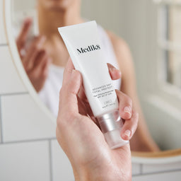 a model holding medik8 advanced day total protect in front of a mirror