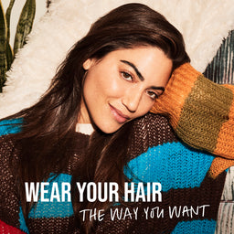 Woman with long hair leaning against a textured surface with text 'WEAR YOUR HAIR THE WAY YOU WANT'.