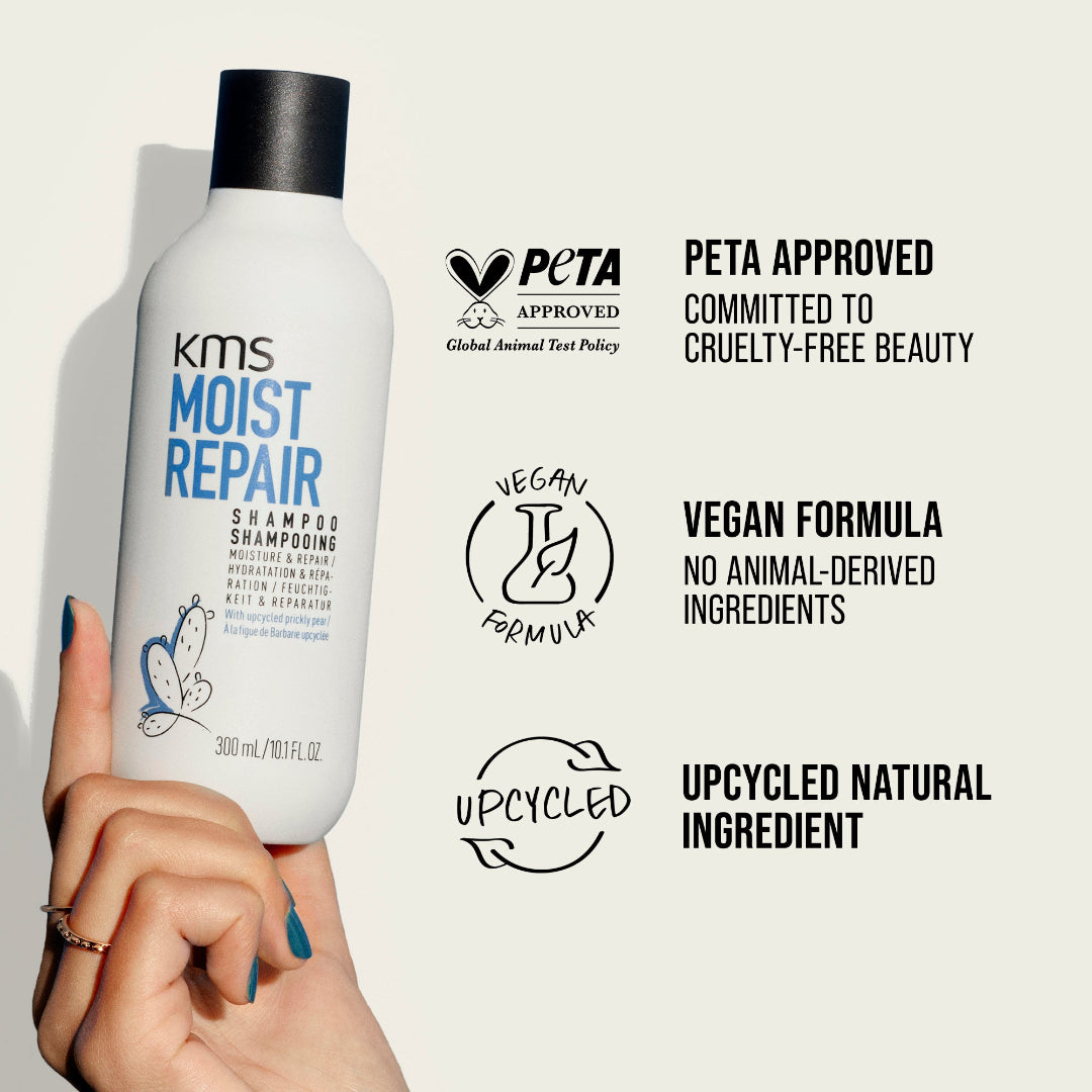 KMS Moist Repair shampoo bottle held by a hand, with PETA approval and vegan formula labels on a light gray background.