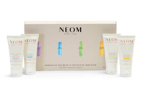 NEOM Moments of Wellbeing in the Palm of Your Hand gift set, featuring a beige presentation box with four small white hand cream tubes arranged in front on a white background.