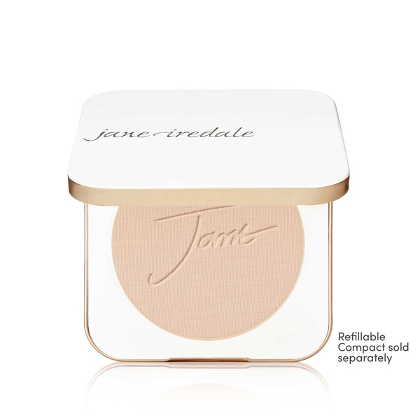 A Jane Iredale makeup compact with a white lid and a clear base showing a round blush or pressed powder in a light peach-beige shade. The compact has a thin metallic gold frame.