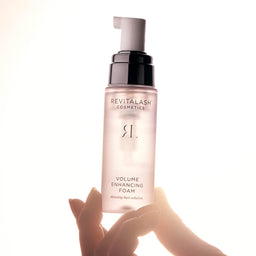 Revitalash Volume Enhancing Foam bottle held by a hand on a white background
