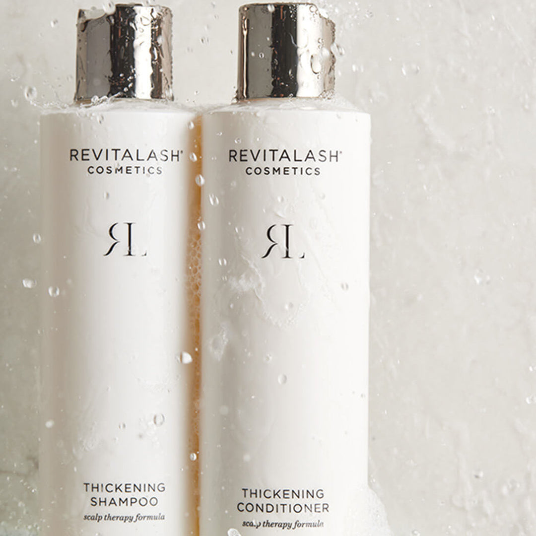 Two Revitalash Cosmetics bottles on a glass surface with water droplets.