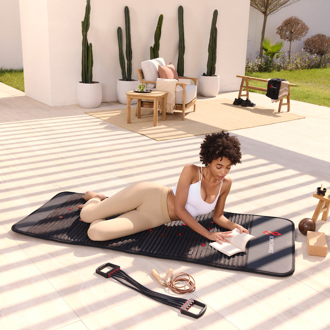 Woman lying on a black mat outdoors with plants and furniture in the background