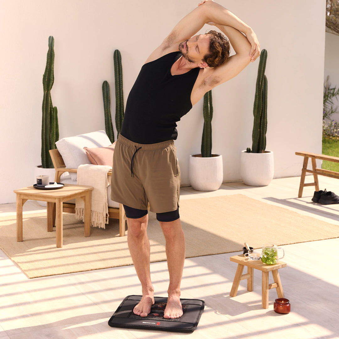 Man exercising on a vibration plate in a home setting with cacti and furniture.