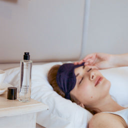a bottle of Olverum Restful Sleep Pillow Mist on a night stand as a women sleeps