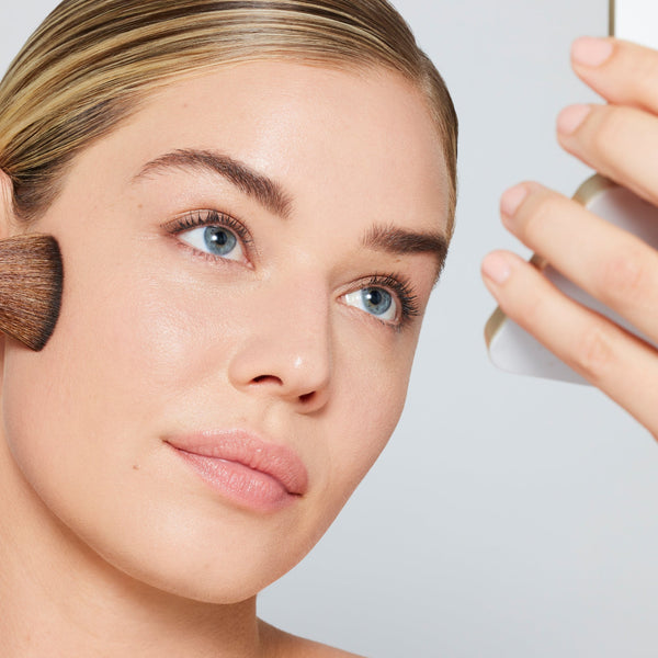Woman applying makeup with a brush on a light gray background