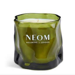 A NEOM Wellbeing London scented candle in a wavy, translucent olive green glass jar, shown on a clean white background.